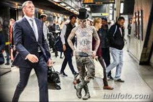 Фото тату мужчины с татуировкой черепа на лице, стоящего в толпе на станции метро. Черно-белое изображение с реалистичной проработкой деталей.